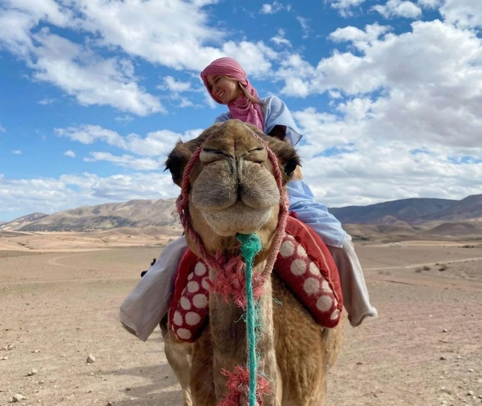 Close-up of a rider smiling on a camel with the Agafay Desert hills behind