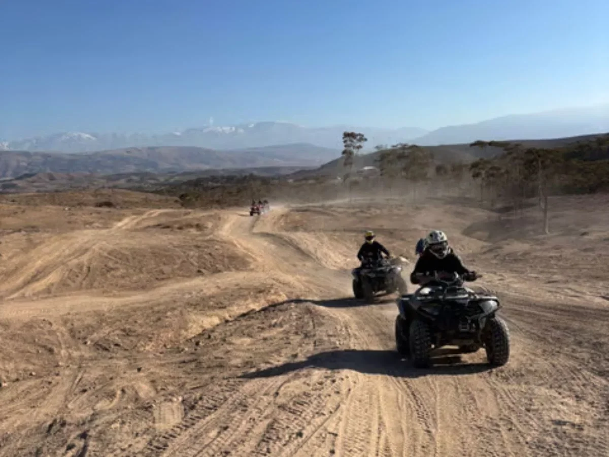 Quad bikers riding along a dusty desert trail with mountains in the distance