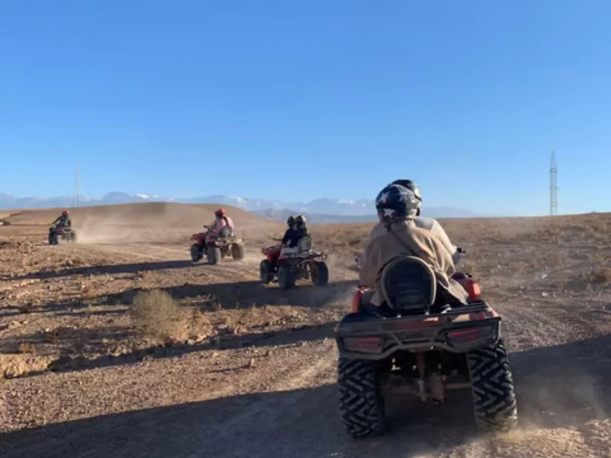 Three riders on quad bikes crossing a desert trail in the Agafay Desert